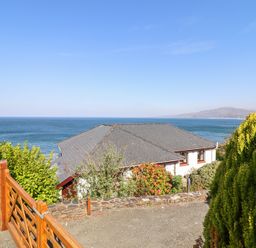 A house with a pitched roof by the sea with a wooden gate and greenery at Gwylanod in Llwyngwril near Fairbourne