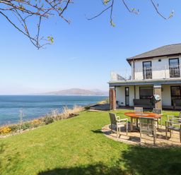 A house with a patio set on a grassy lawn overlooking the sea at Gwylanod in Llwyngwril near Fairbourne