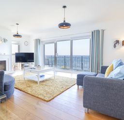 A living room with grey sofas a white coffee table a yellow rug a fireplace and large windows with sea view at Gwylanod in Llwyngwril near Fairbourne