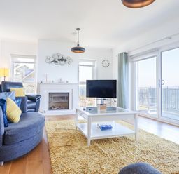 A living room with sofas, a coffee table, a television, a fireplace, and large windows at Gwylanod in Llwyngwril near Fairbourne