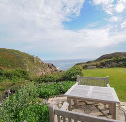A garden area with wooden table and chairs overlooking the ocean at Pendower Cottage in Porthgwarra