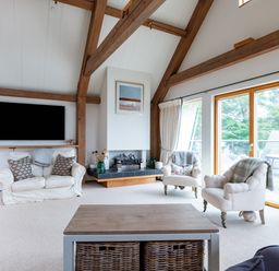 A living room with wooden beams television fireplace armchairs and large windows at Gull Rock 4 Rock