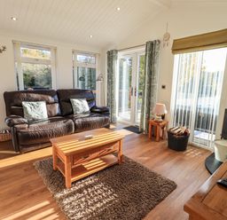 A living room with a brown leather sofa a wooden coffee table a rug and a wood stove at Pippin Lodge in Allithwaite near Cartmel
