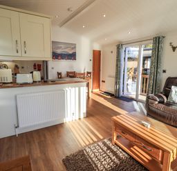 A living room with a brown leather sofa a wooden coffee table and a dining table near the kitchen at Pippin Lodge in Allithwaite near Cartmel