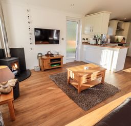 A living room with a wood burning stove wooden furniture and an open kitchen at Pippin Lodge in Allithwaite near Cartmel