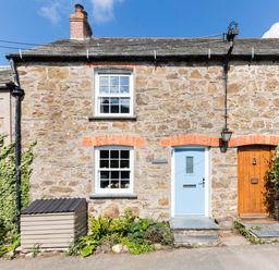 Stone cottage with blue and wooden doors and two windows with plants outside at Stokes Cottage in St Minver