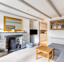 A living room with a stone fireplace a wooden coffee table a gray sofa with yellow pillows and a wall cabinet at Stokes Cottage in St Minver