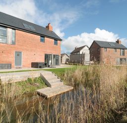 Two brick houses with black roofs near a water body with wooden steps and tall grass at Agua de Plata 16 Wakeling Island Silverlake in Dorchester