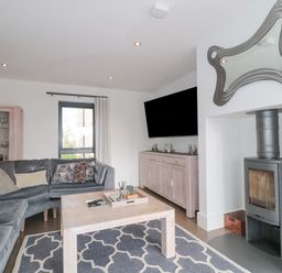 A living room with a grey sectional sofa a wooden coffee table a patterned rug a wall-mounted TV a wood-burning stove and a cabinet with glass doors at Agua de Plata 16 Wakeling Island Silverlake in Dorchester