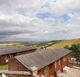 A view of wooden cabins on a hillside with a patio and outdoor furniture surrounded by fields and hills at Tamar View Lodge in Millbrook