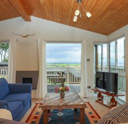 A living room with blue sofa wooden coffee table and television near large windows at Tamar View Lodge in Millbrook