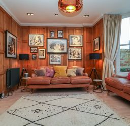 A sitting room with brown leather sofas colourful cushions black lamps and framed photos on wooden paneled walls at 42 Crag Path in Aldeburgh