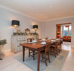 A dining room with a wooden table and chairs a sideboard with lamps and decorations and a living room visible through a doorway at 42 Crag Path in Aldeburgh