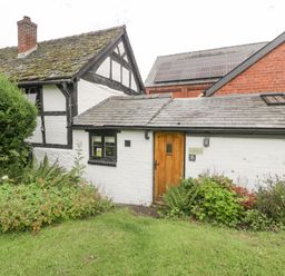 A white brick house with a wooden door surrounded by plants and grass at The Old Bakehouse in Pembridge