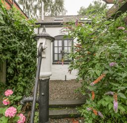 A garden area with an old water pump surrounded by plants and flowers at The Old Bakehouse in Pembridge