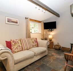 A living room with a beige sofa and patterned cushions a wall-mounted TV and a wood-burning stove at The Old Bakehouse in Pembridge