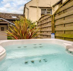 An outdoor hot tub with water next to a wooden fence and a stone building at Shepherds Cottage in Hawkshead