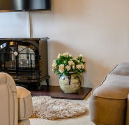 A black stove heater with a vase of white flowers next to it and beige armchairs in a living room at Shepherds Cottage in Hawkshead