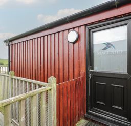 An exterior red wooden building with a black door labeled Mallard and a wooden railing surrounding a walkway at Mallard Lodge in Moscow near Galston