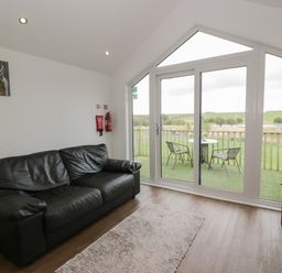 A living room with a black leather sofa a rug and glass doors opening to a balcony with chairs and a table at Mallard Lodge in Moscow near Galston