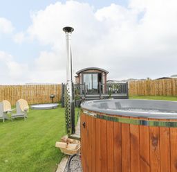 A garden with a wooden hot tub chairs and a small wooden house behind a fence at Greenacres Carriage in Maybole