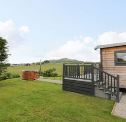 A wooden cabin with a small porch and steps next to a grassy yard and a round wooden hot tub at Greenacres Carriage in Maybole