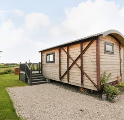 A wooden cabin on gravel with steps and railing surrounded by grass at Greenacres Carriage in Maybole