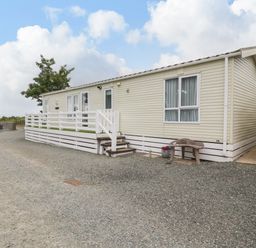 A beige mobile home with white railings and steps on a gravel driveway at Gwel Eryri in Penmynydd near Llanfairpwllgwyngyll