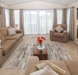 A living room with brown sofas a coffee table with flowers a wall mounted television and large windows at Gwel Eryri in Penmynydd near Llanfairpwllgwyngyll