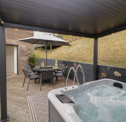 A covered outdoor patio with a hot tub and dining table under an umbrella at 12 Beachdown in Challaborough