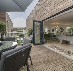 An outdoor patio with a glass table and chairs opening into a room with a pool table and modern lighting at 12 Beachdown in Challaborough