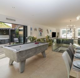 A game room with a pool table dining table set and sofas with large windows and an outdoor seating area at 12 Beachdown in Challaborough
