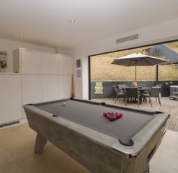 A room with a pool table and white cabinets opening to an outdoor patio with a table umbrella and chairs at 12 Beachdown in Challaborough