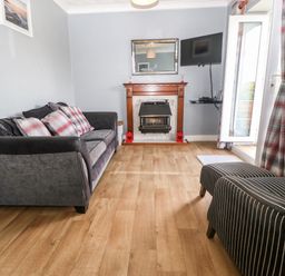 A living room with a sofa armchair fireplace wall mounted tv and open door with curtains at Coed y Glyn Bach Equestrian in Penygroes