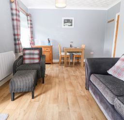 A living room with a sofa and armchair with footstool a wooden dining table with four chairs and a wooden sideboard at Coed y Glyn Bach Equestrian in Penygroes