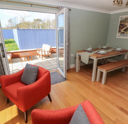 A dining room with table set for four and red chairs next to an open door leading to a patio at The Annexe Meadow Croft in Haverfordwest
