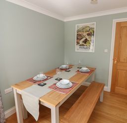 A dining room with a wooden table set for four and a Wales poster on the wall at The Annexe Meadow Croft in Haverfordwest