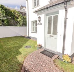 An exterior view of a house entrance with a green door and a brick path surrounded by grass at 3 Strawberry Close in Little Haven near Broad Haven