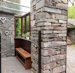 A stone entrance area with a wooden bench plants on a window ledge and heart decorations on the wall at Holly Cottage in Grasmere