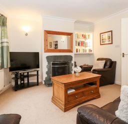 A living room with a wooden coffee table leather sofas a TV on a stand a fireplace and bookshelves at Holly Cottage in Grasmere