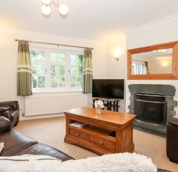 A living room with a wooden coffee table a fireplace and a television at Holly Cottage in Grasmere