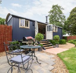 A garden with a metal table and chairs set on a stone patio outside a small blue cabin at Utopia in Metfield near Harleston