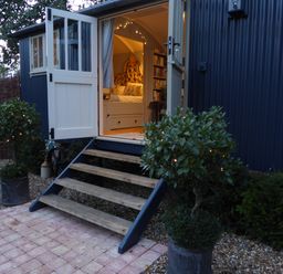 An open doorway with wooden steps leading to a bedroom inside a dark blue building with potted plants and string lights outside at Utopia in Metfield near Harleston