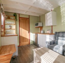A small kitchen area with a wooden door plaid armchair wooden countertop and microwave at Nyth Y Bioden (Magpie's Nest) Llanaelhaearn near Trefor