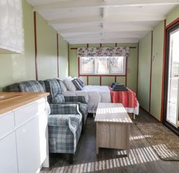 A small living area with a bed, two armchairs, a coffee table, kitchenette, and glass doors at Nyth Y Bioden (Magpie's Nest) in Llanaelhaearn near Trefor