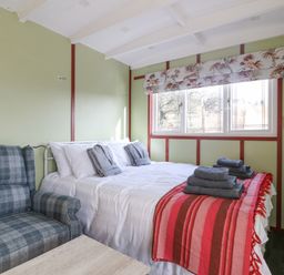 A bedroom with a bed covered in white linens and gray towels a plaid armchair and a window with floral blinds at Nyth Y Bioden (Magpie's Nest) in Llanaelhaearn near Trefor