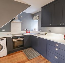 A kitchen with dark cabinets a white washing machine oven sink toaster and kettle at Grebe Cottage in Alnmouth