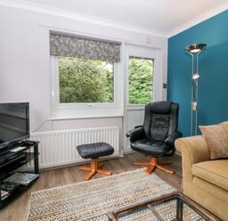 A living room with a black leather chair with footrest a yellow sofa a floor lamp and a television on a stand at The Lodge in Ambleside