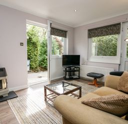 A living room with a beige sofa and a glass coffee table near a TV and open door at The Lodge in Ambleside