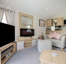 A living room with a sofa and ottoman next to a wood entertainment unit with a mounted electric fireplace and a television at Pams Place in Crantock